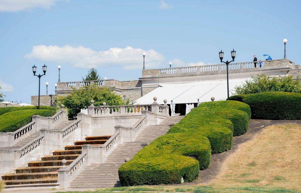 Historic white stone staircase with ornate railings and lamp posts leads up a grassy hill to a grand plaza overlook.