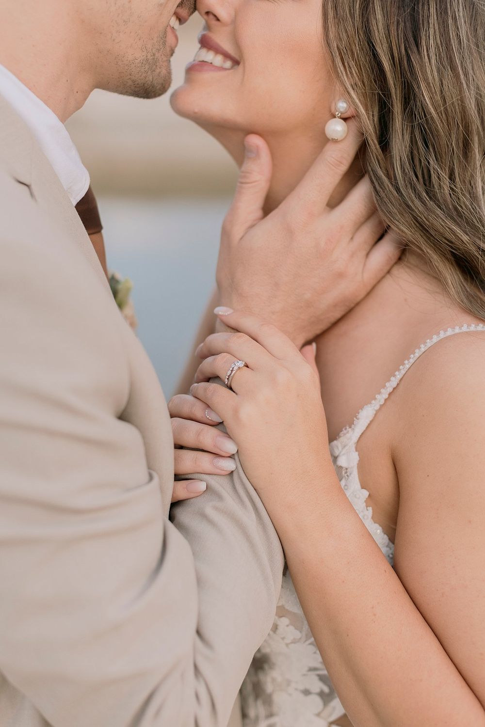 Intimate close-up of bride and groom almost kissing highlighting her diamond ring and pearl drop earring.