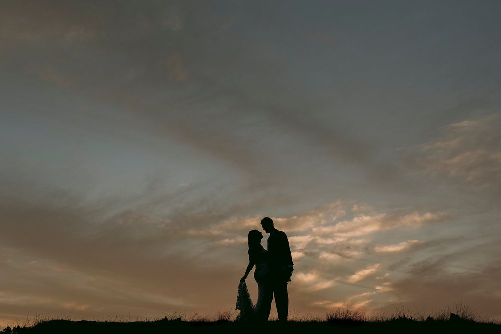 Romantic silhouette of bride and groom facing each other against a stunning golden sunset sky.