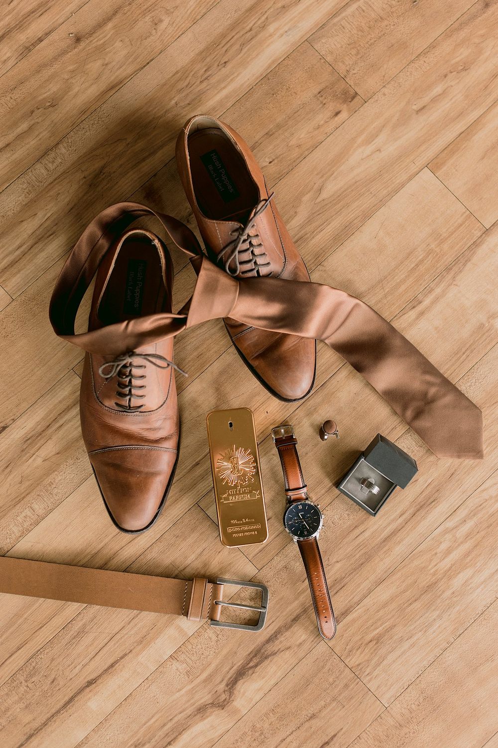 Grooms wedding accessories flat lay with tan leather shoes, silk tie, watch, and cologne.