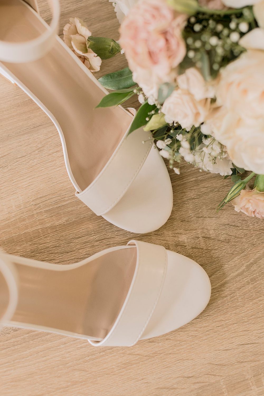White block heel bridal sandals placed in front of a soft pink and white wedding bouquet.