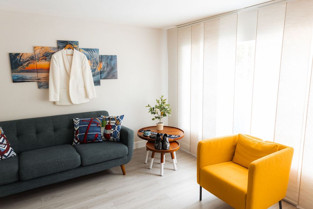 Modern living room featuring a navy sofa, yellow accent chair, and multi-panel wall art in a bright, minimalist space.