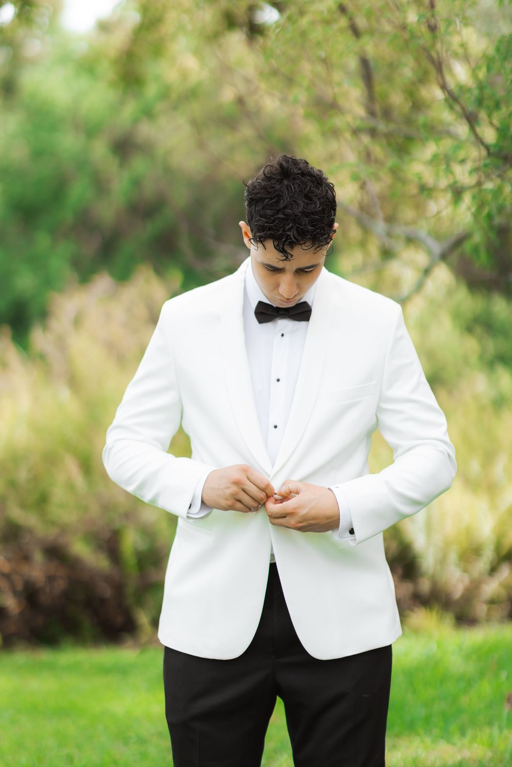 A formal outfit featuring a crisp white dinner jacket with black bow tie and trousers in an outdoor garden setting.