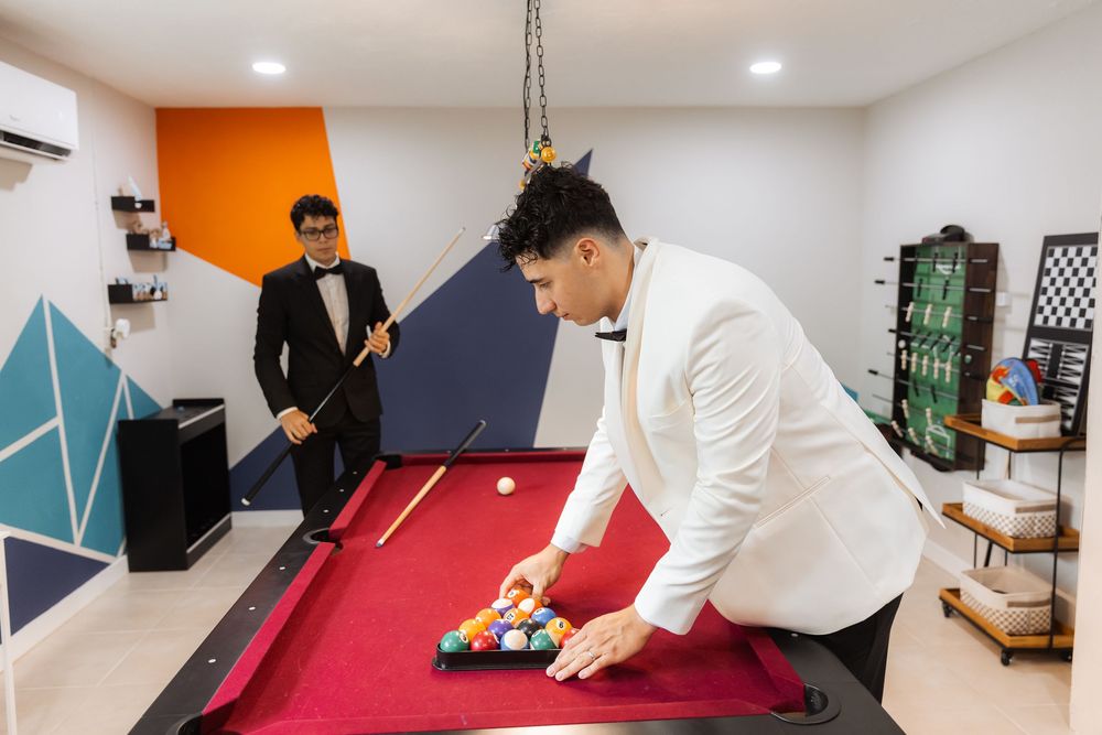 Two people playing pool in a modern game room with orange and blue accent walls and floating shelves.