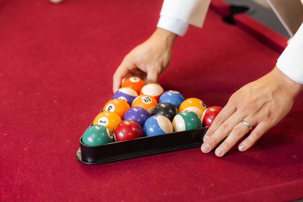 Hands racking up colorful pool balls in a triangle rack on a red felt billiards table.