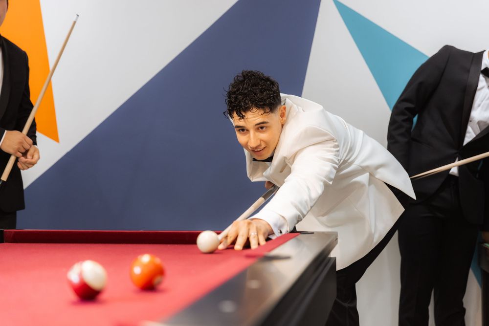 Young person in white shirt lines up shot while playing pool at modern entertainment venue with geometric wall decor.