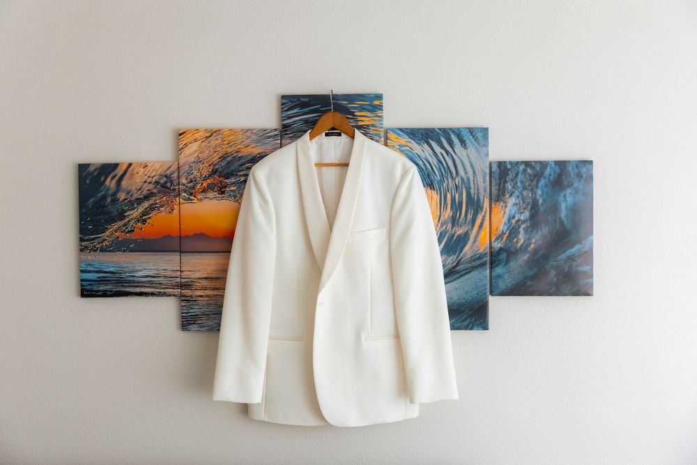 A white blazer jacket hangs on a hanger against a wall with colorful ocean wave artwork panels in the background.