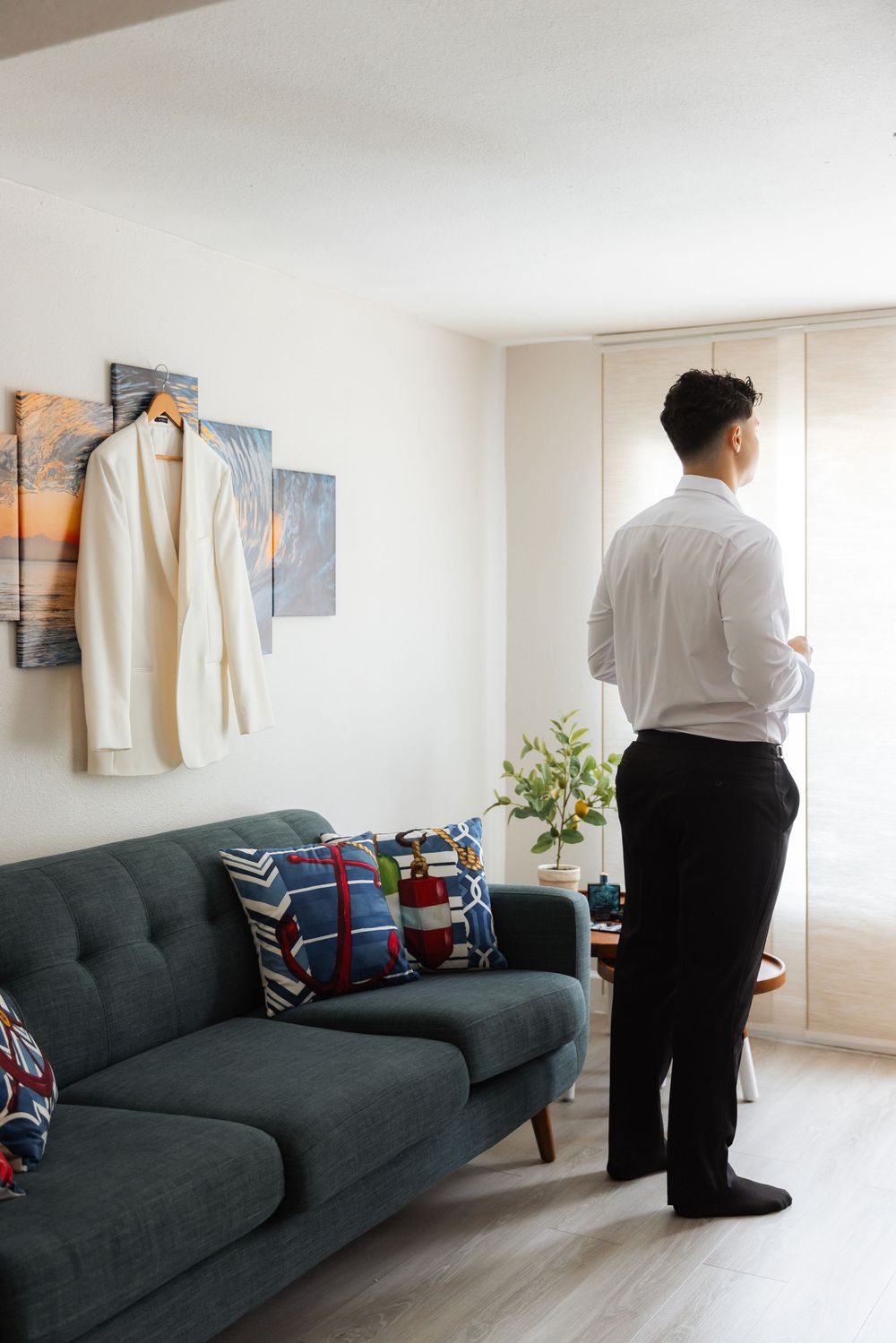 Modern living room interior with dark grey sofa, decorative pillows, wall art, and person standing by window.