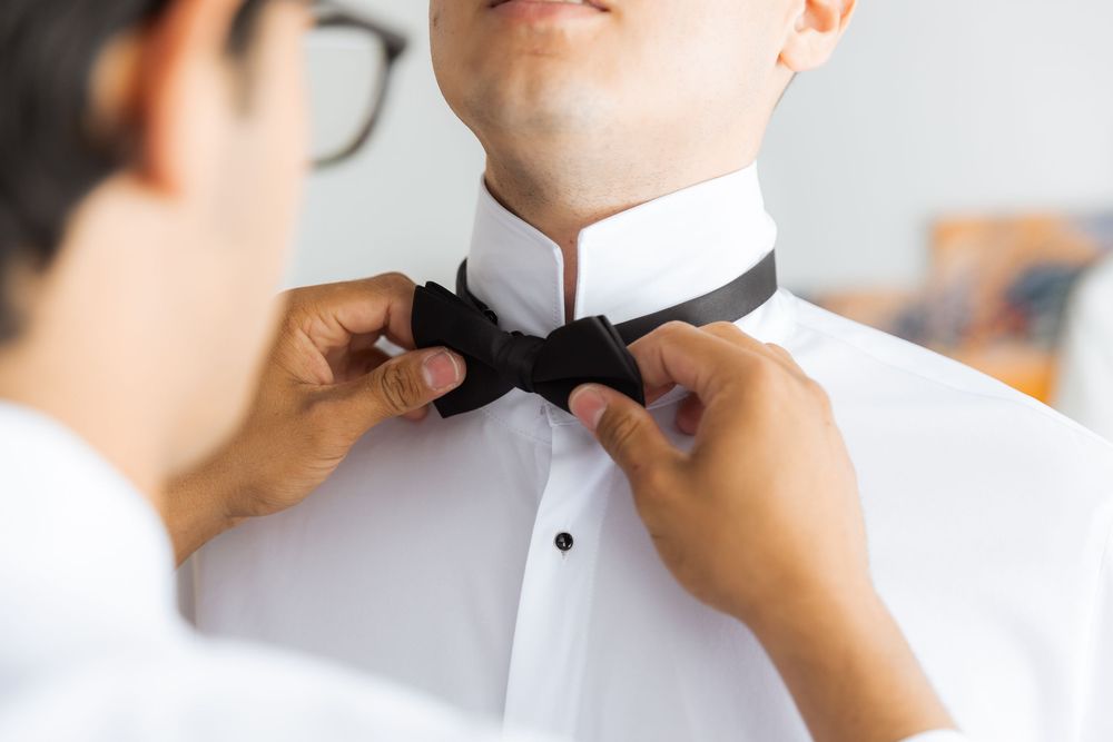 Hands adjusting a black bow tie on a crisp white formal dress shirt before an event.