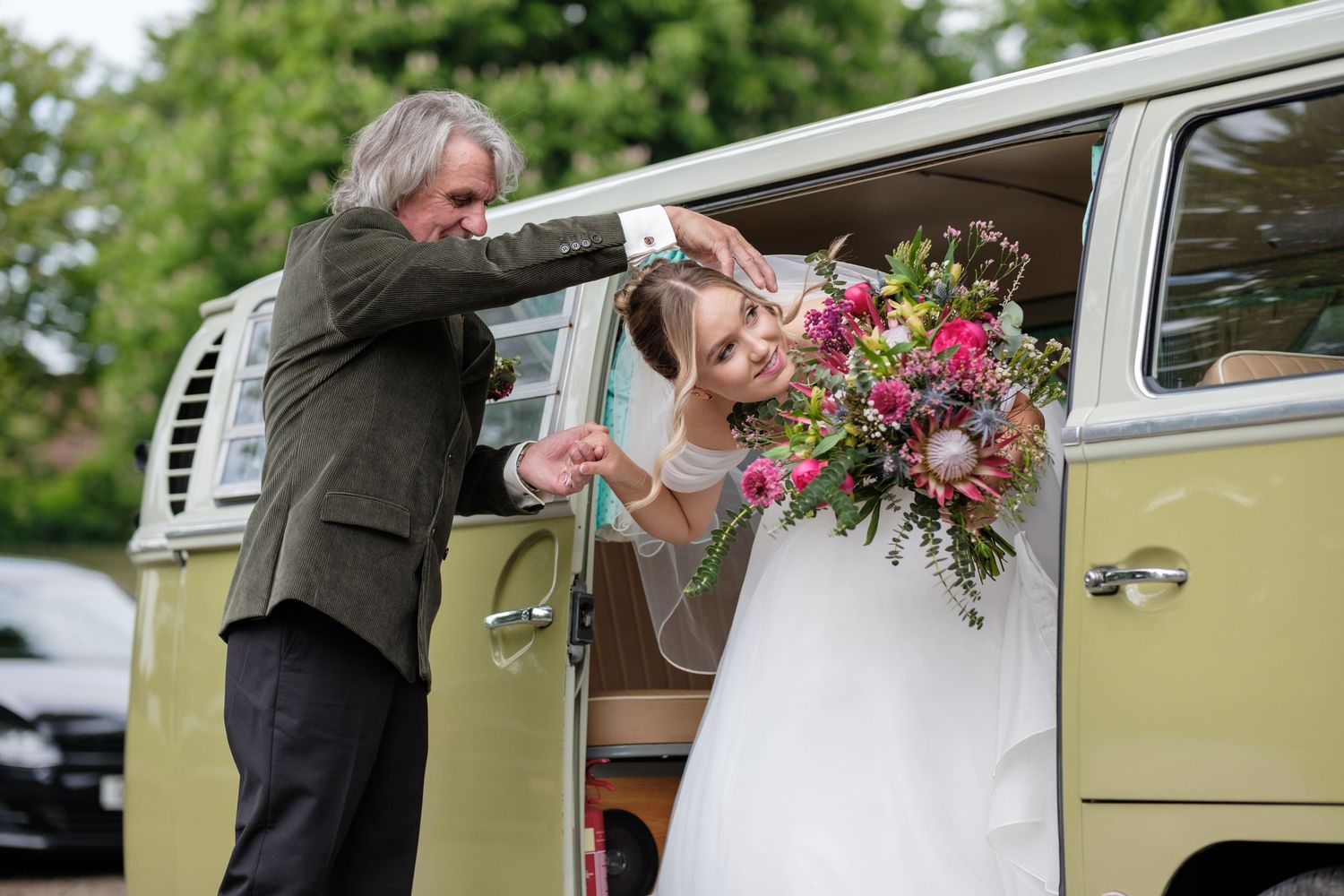 A vintage VW van serves as wedding transport while bridal bouquet of vibrant flowers is held.