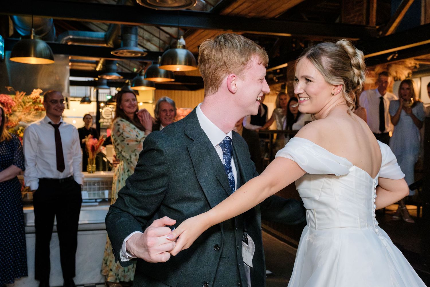 A couple shares their first dance together at their wedding reception in a rustic venue with exposed ceiling beams.