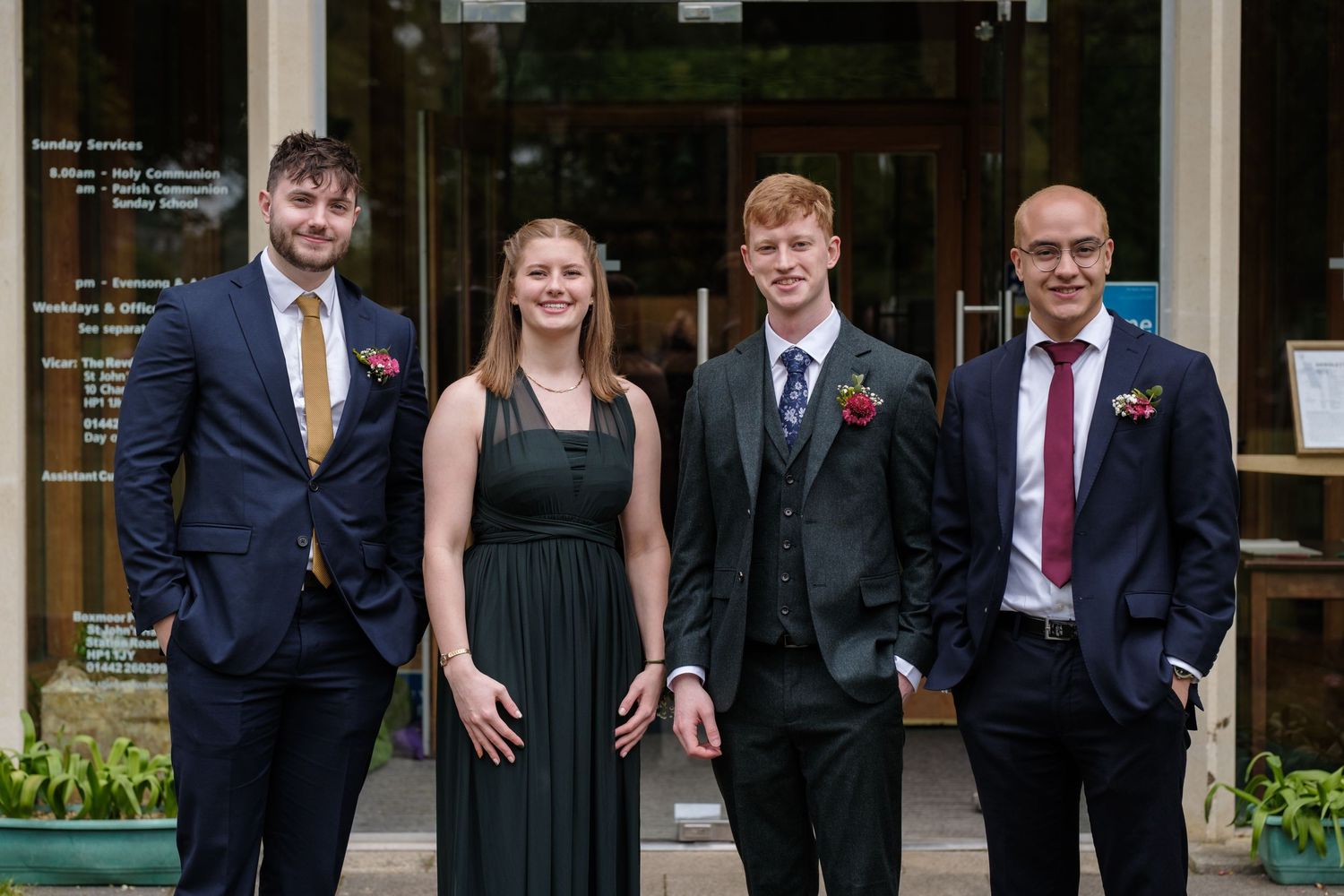 Small wedding party in formal attire poses together outside a building.