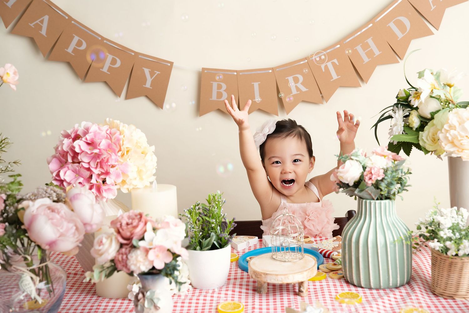Elegant first birthday setup with pink and white decor, flowers, and rustic banners.