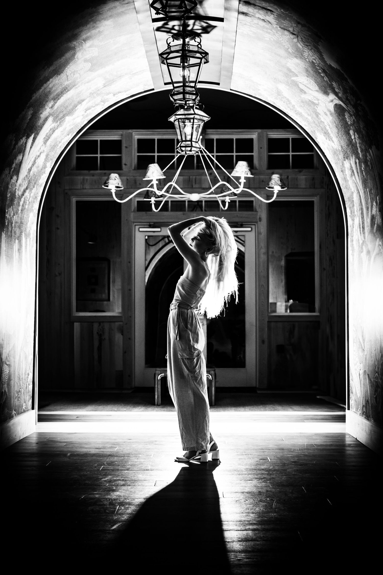 A silhouetted figure stands gracefully in an arched doorway beneath an ornate chandelier in dramatic lighting. Charleston Photographer