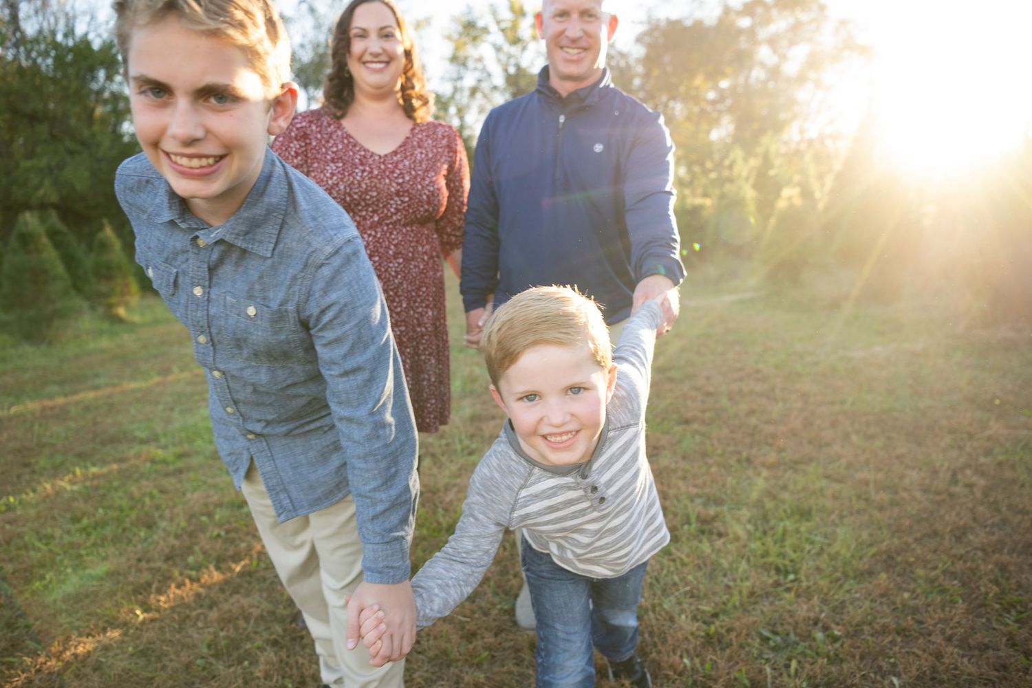 Family walking through field at sunset with children leading the way at a Christmas tree farm in Columbia, TN.