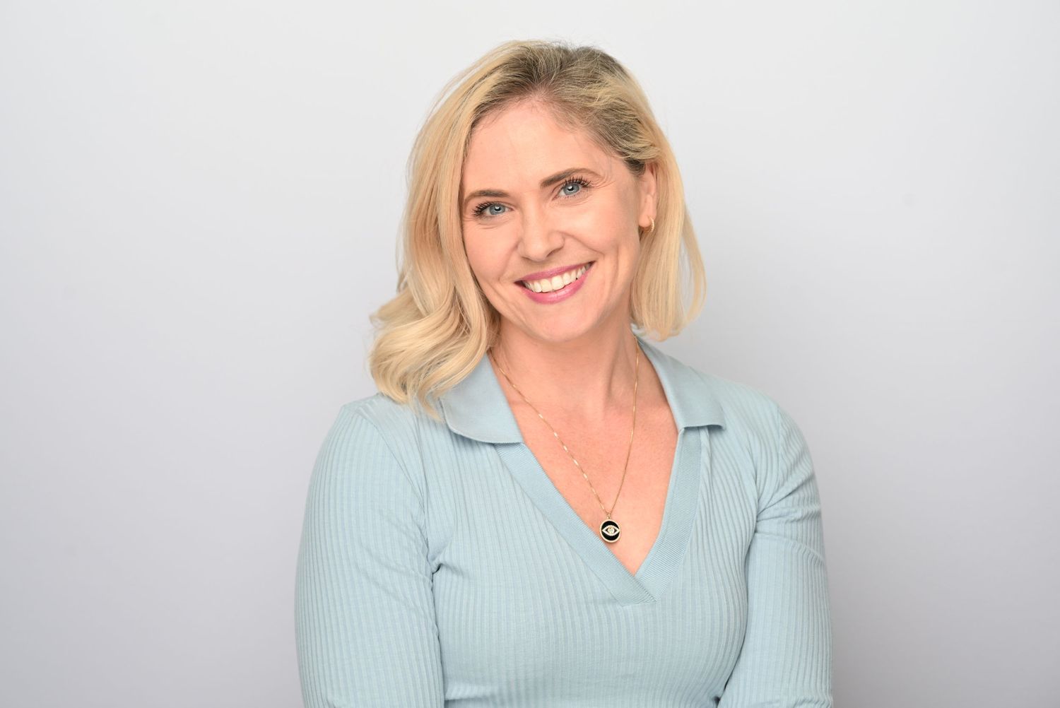 Professional headshot portrait against a light blue background wearing a black blazer and smiling warmly.