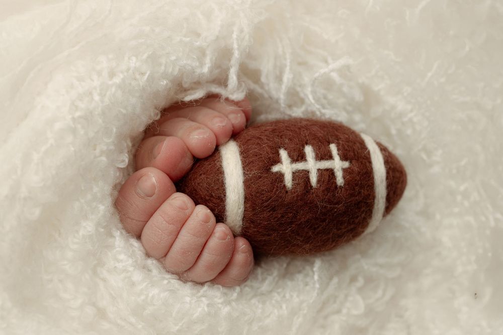 Five sequential photos showing the creation of a miniature football made from brown and white yarn. – newborn photographer Paloma Schell