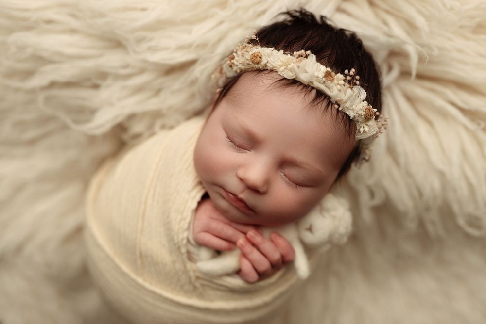 Sleeping newborn baby wearing cream-colored wrap and delicate lace headband in soft lighting – newborn photographer Paloma Schell Houston TX