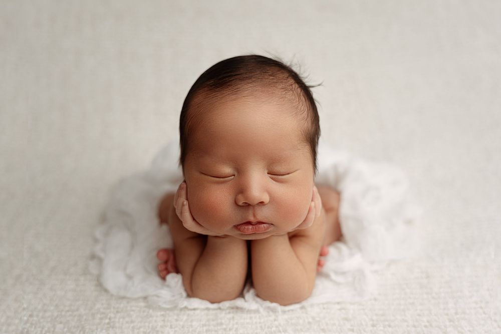 Sleeping newborn baby rests peacefully on soft white blanket in professional studio portrait– newborn photographer Paloma Schell Houston TX