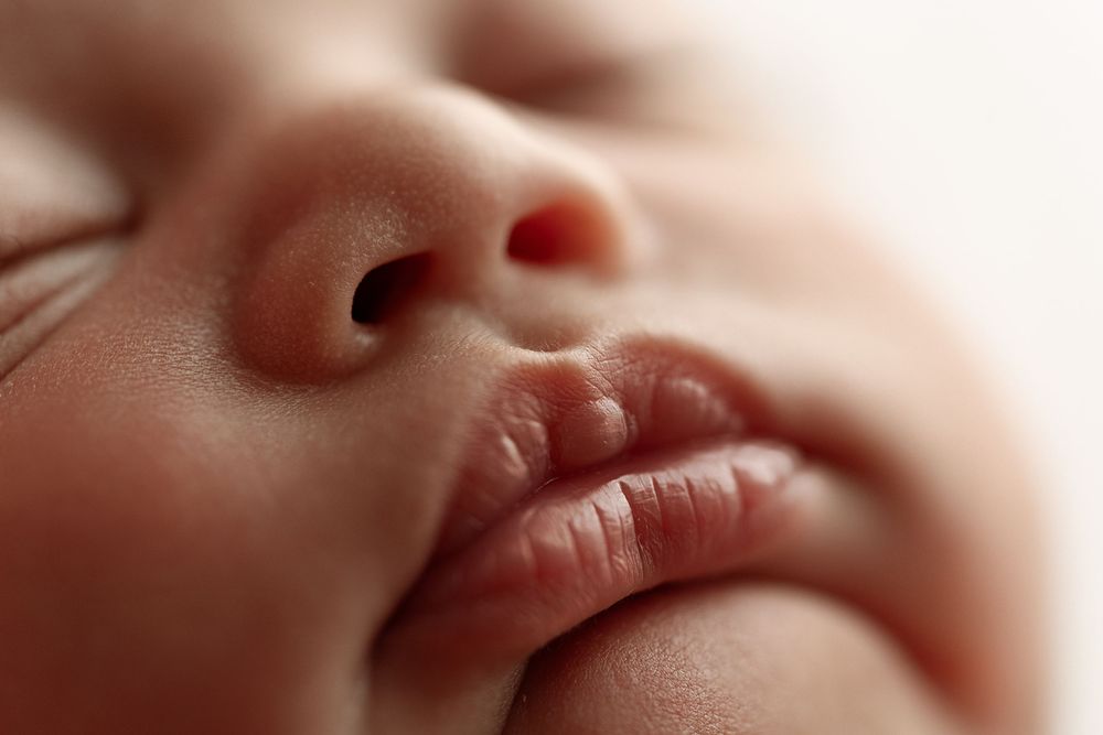 Close-up of a sleeping newborn baby's delicate facial features against a soft white background.– newborn photographer Paloma Schell Houston