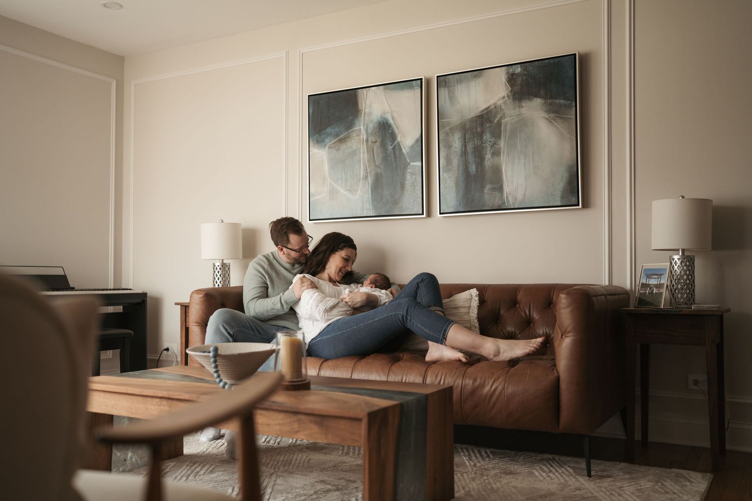 A couple lounges together on a brown leather couch holding their newborn during a newborn session