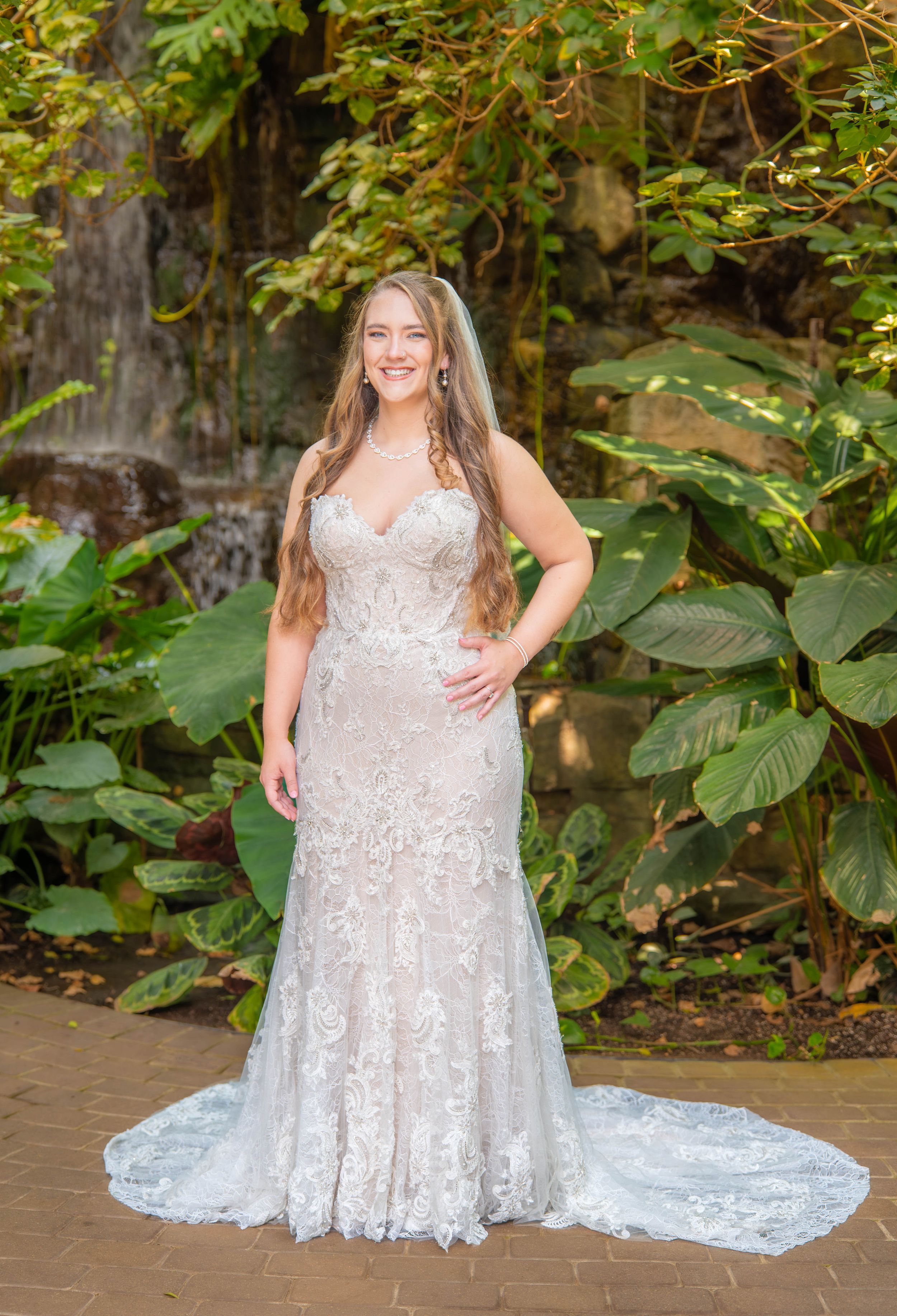 Full-length bridal portraits showing detailed lace wedding gown with train in garden setting.