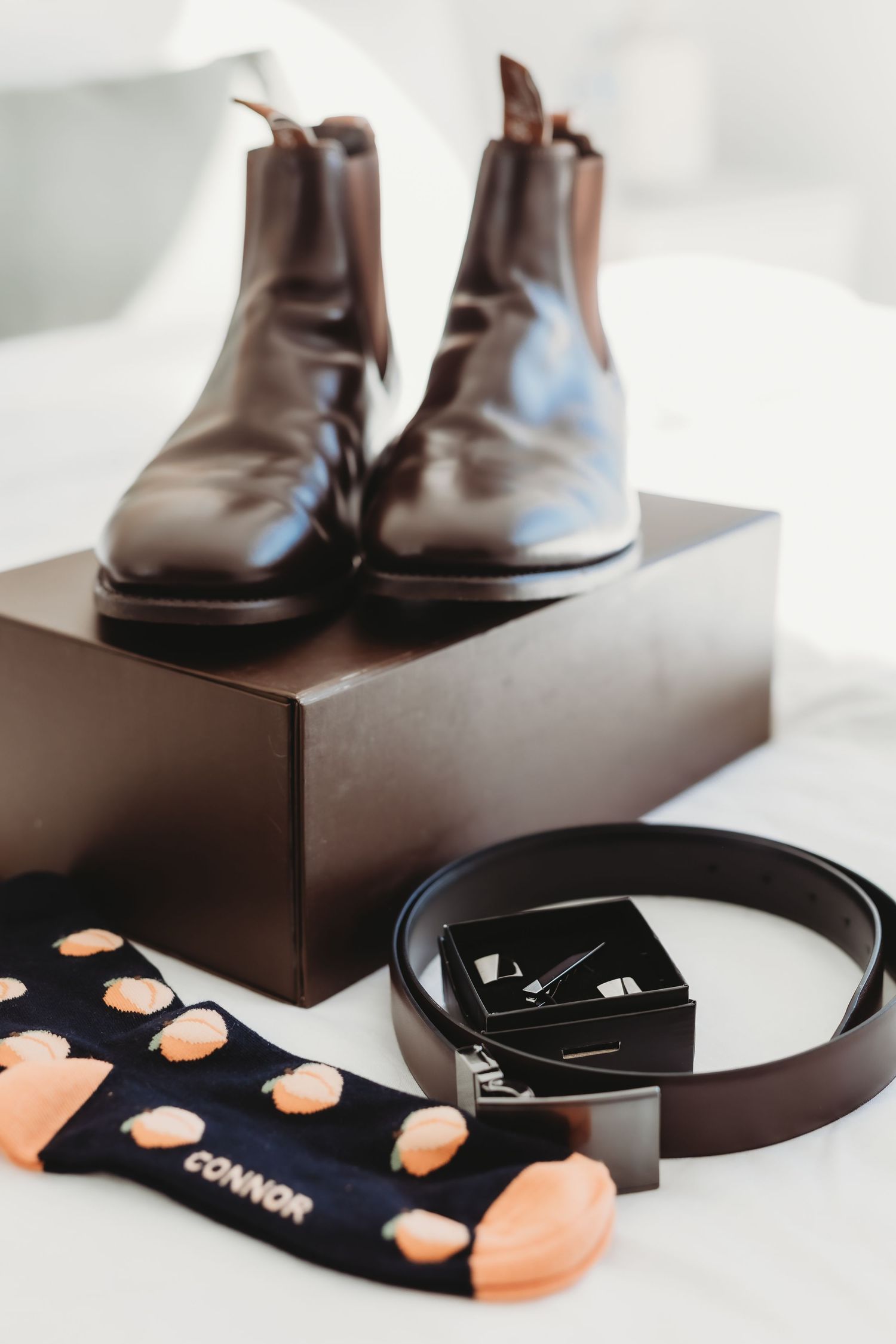 Brown leather dress shoes and black socks arranged on dark boxes against a white background.