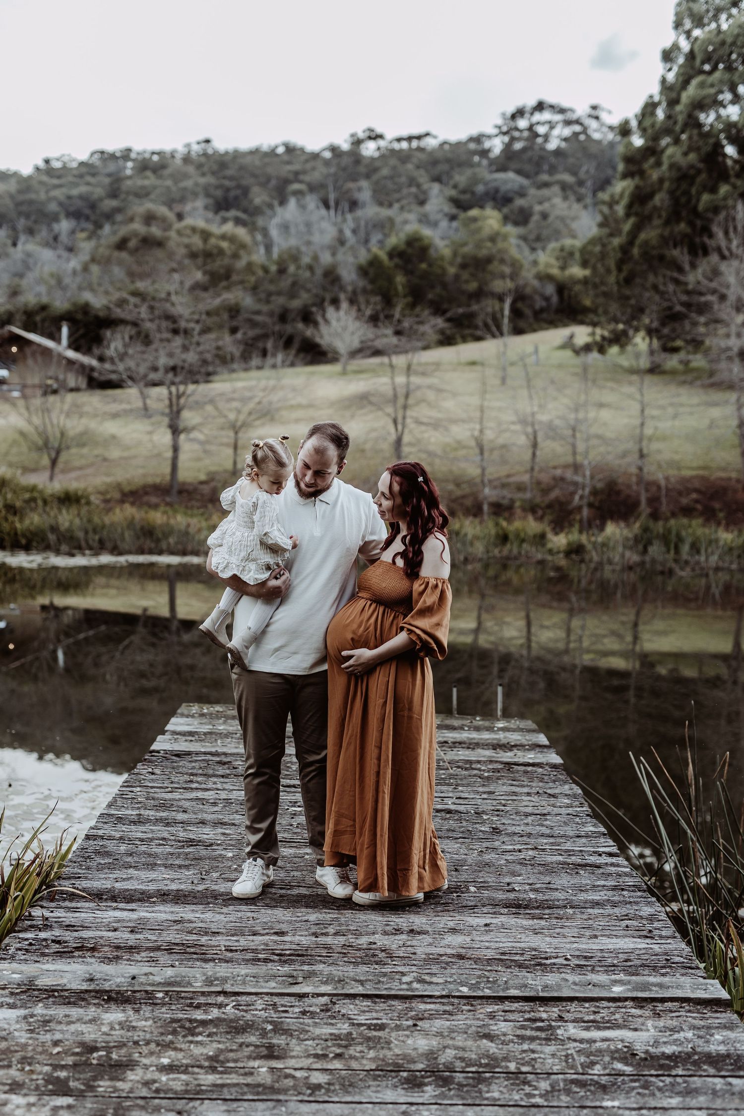 Family standing together on a wooden dock overlooking a serene lake at dusk.