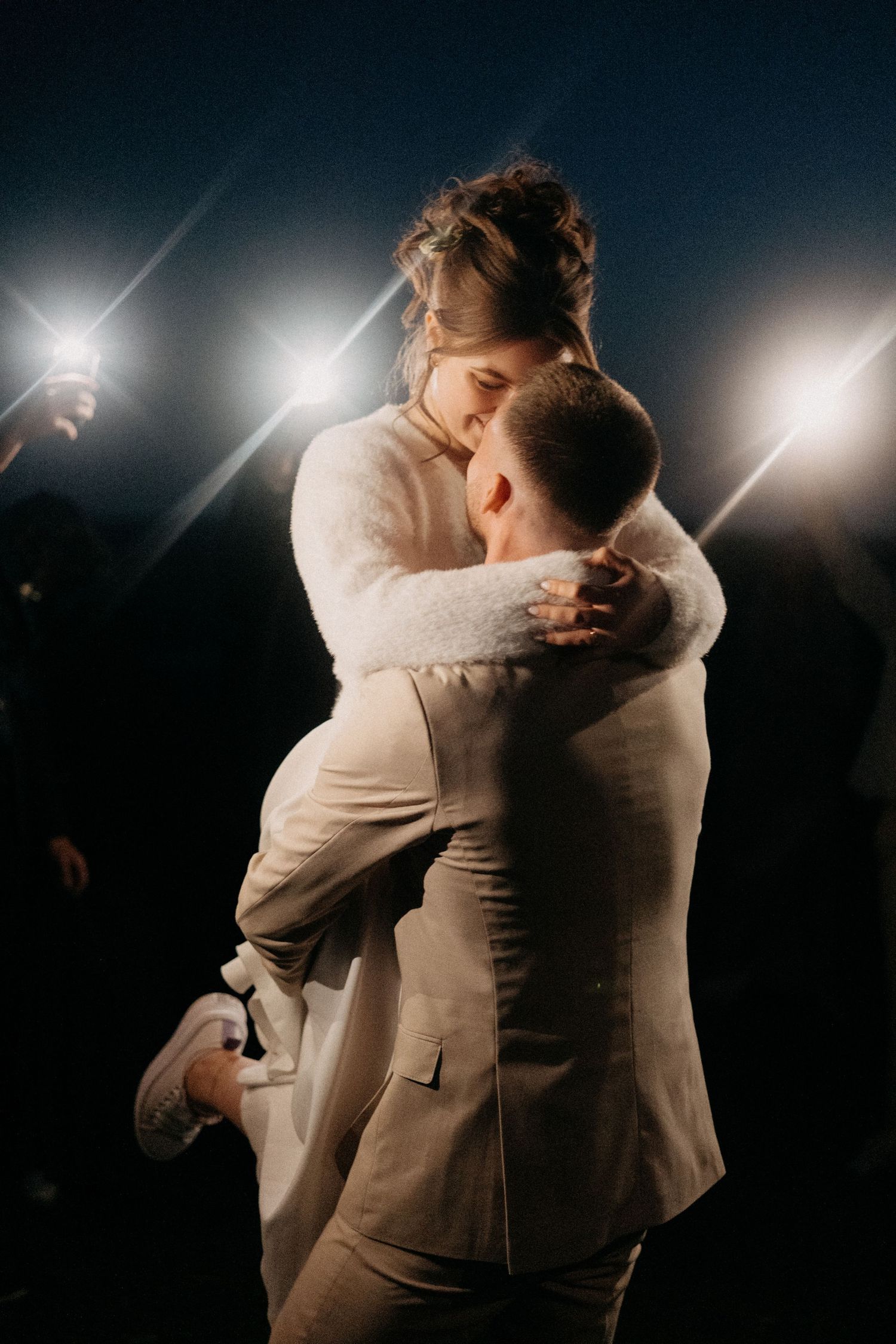 Dramatic nighttime dance scene with couple embracing under spotlights at wedding reception.