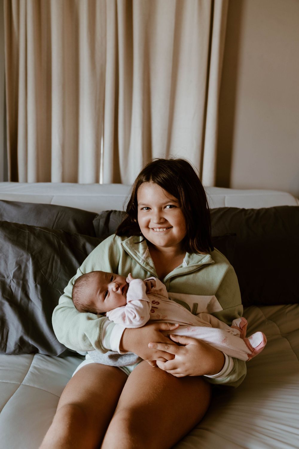 A tender moment of bonding with a newborn baby on a gray couch in natural lighting.