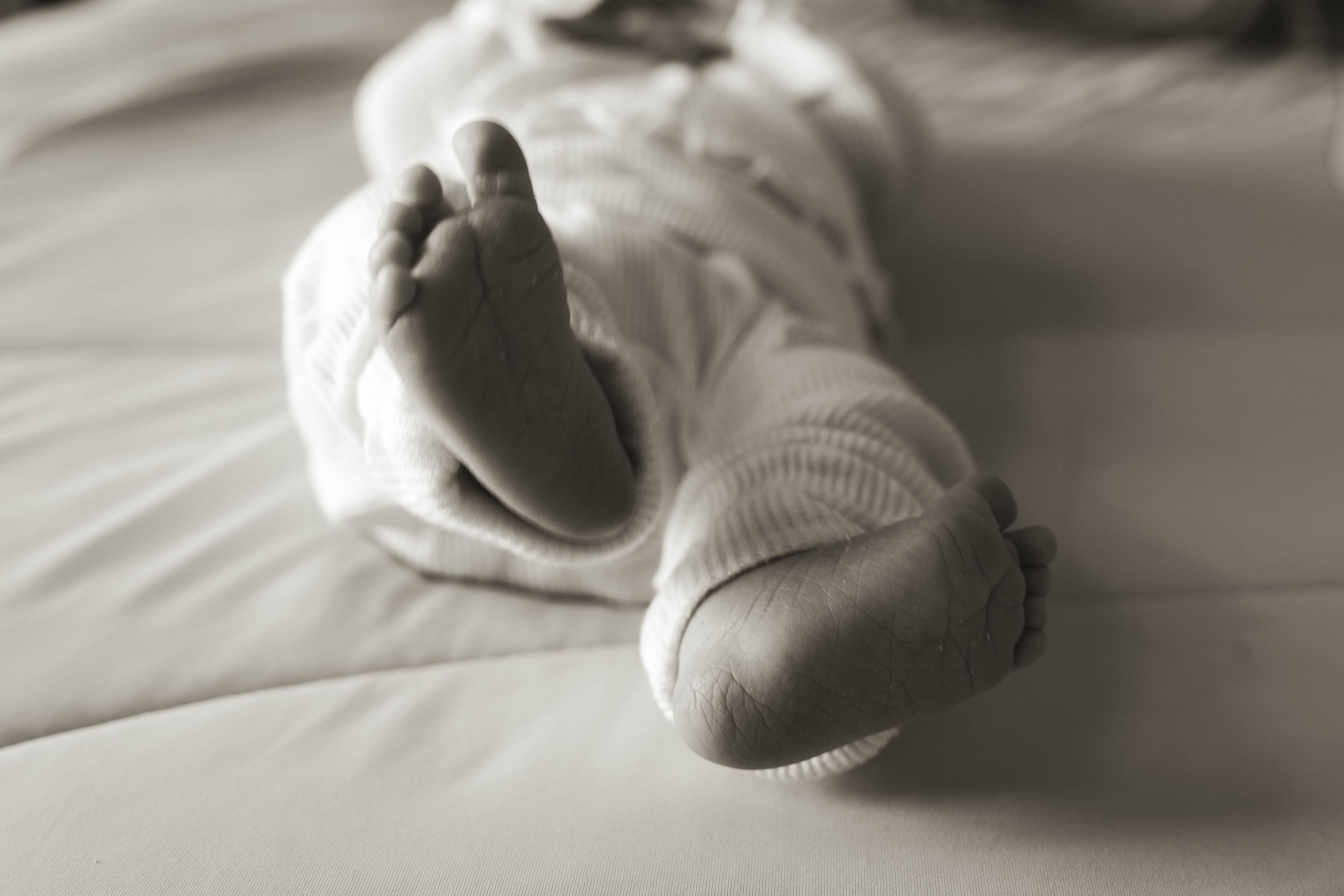 Minimalist black and white image of a sleeping newborn on white sheets.