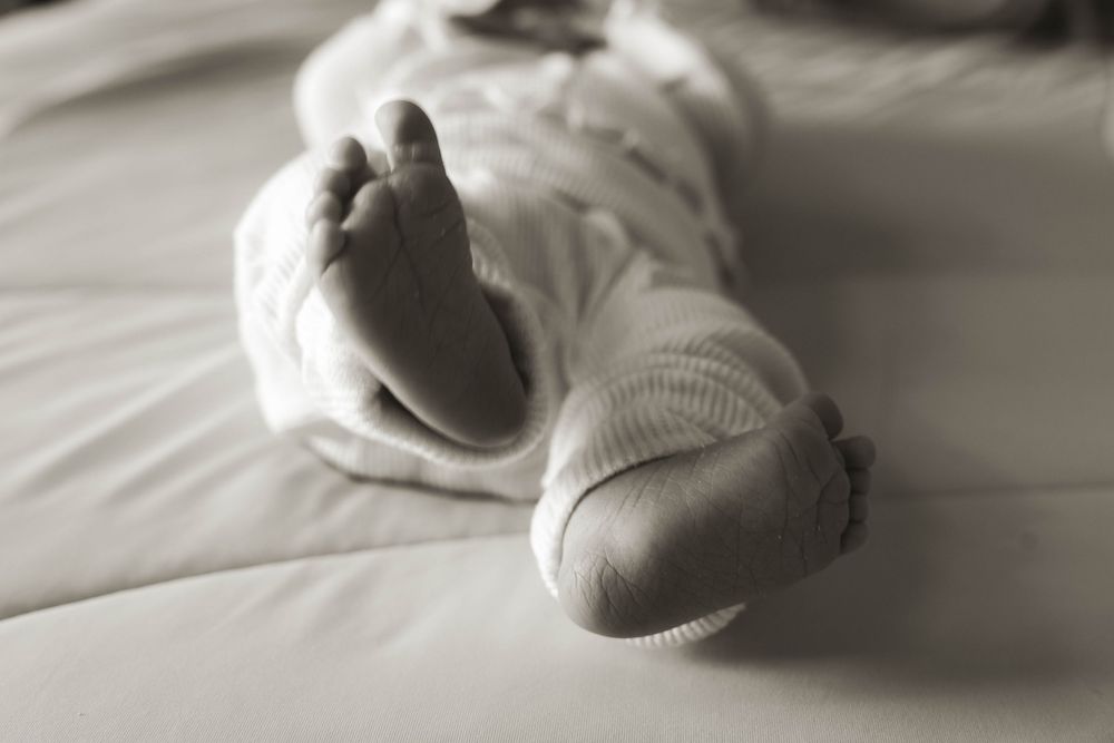 Minimalist black and white image of a sleeping newborn on white sheets.