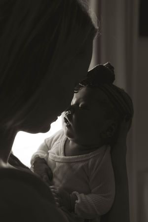 Silhouetted figures in front of window share intimate family moment with newborn in dramatic lighting.