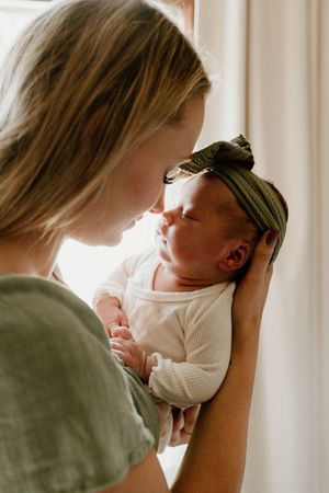 Parent tenderly holds and gazes at newborn baby near sunlit window.