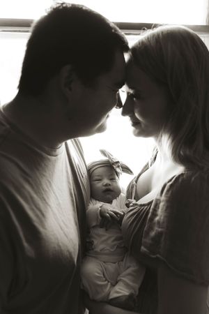 Family captures tender moments with newborn in dramatic window lighting.
