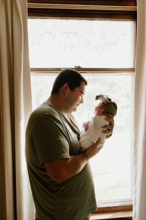 Parents sharing loving moments with their newborn baby near a bright window.