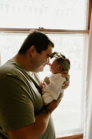 Tender family moment captured in warm light as parents cradle their newborn by a window.