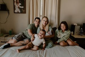 Family relaxing together on white bedding during casual lifestyle photo session.