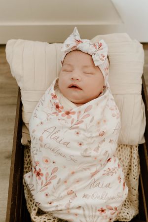 Sleeping newborn wrapped in floral swaddle blanket with name Maia.