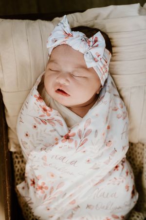 Close-up shots of sleeping newborn in floral swaddle and matching bow headband.