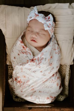 Sleeping newborn baby wrapped in floral swaddle blanket with delicate bow headband.
