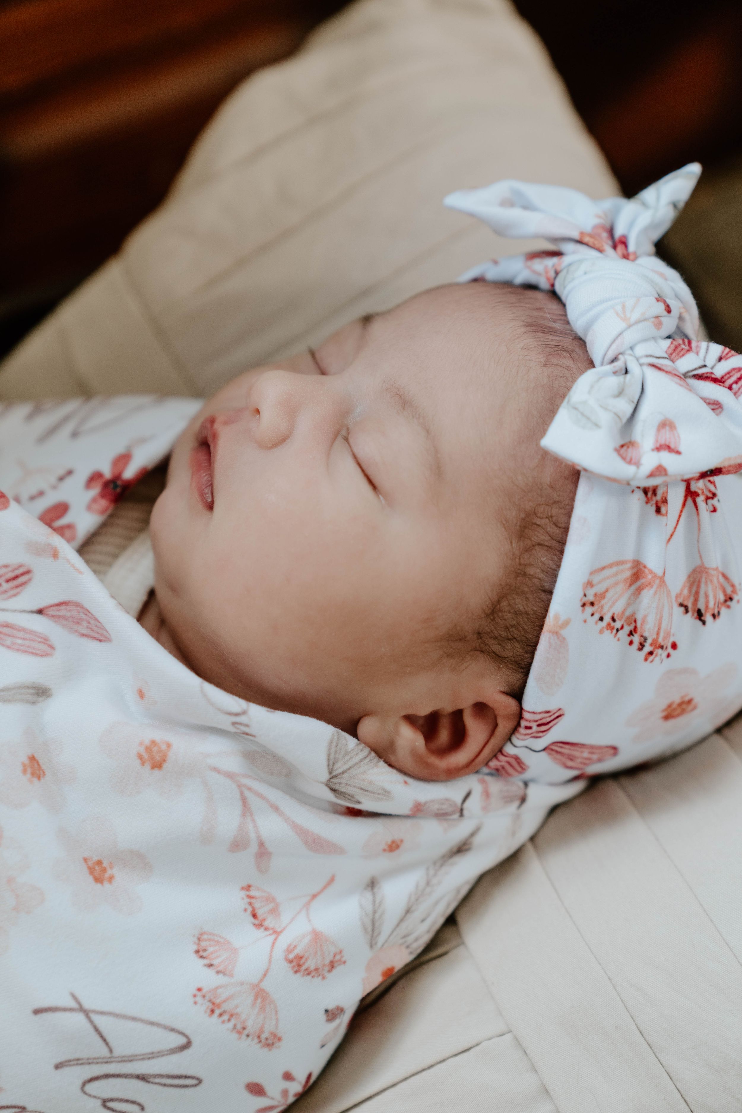 Peaceful newborn baby resting in white and coral floral swaddle blanket.