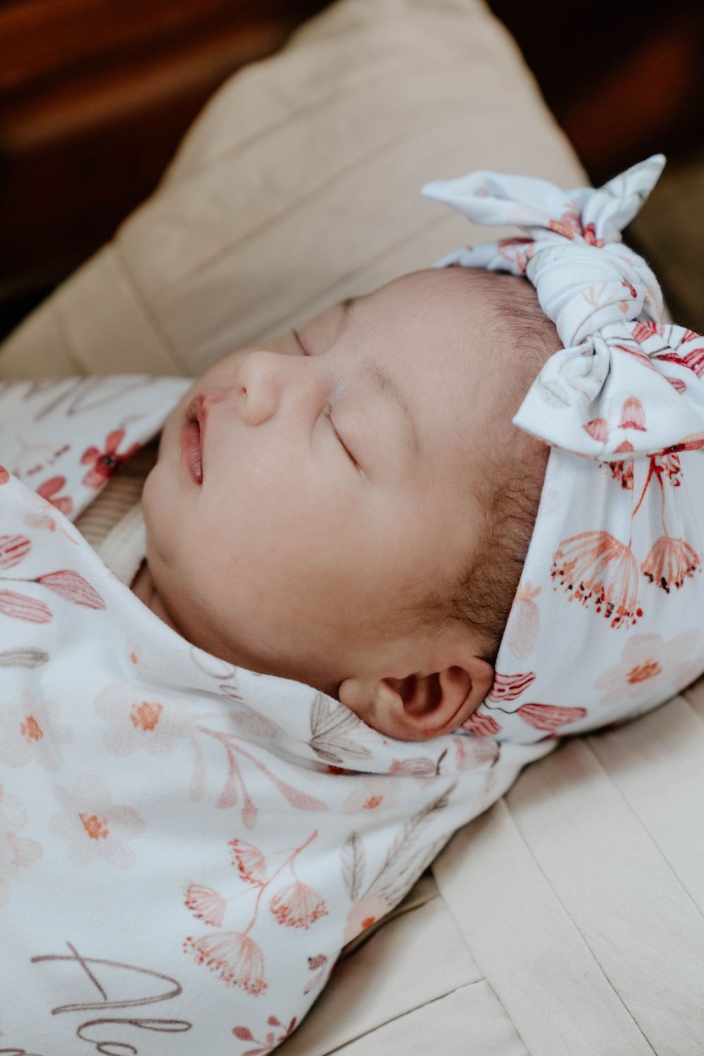 Peaceful newborn baby resting in white and coral floral swaddle blanket.