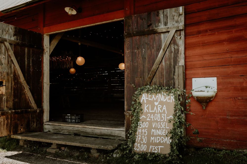 Ingång till festkolal på Näs Herrgård. Programm för festen står på en skylt utanför dörren. Ladan är röd och skylten har vit text.