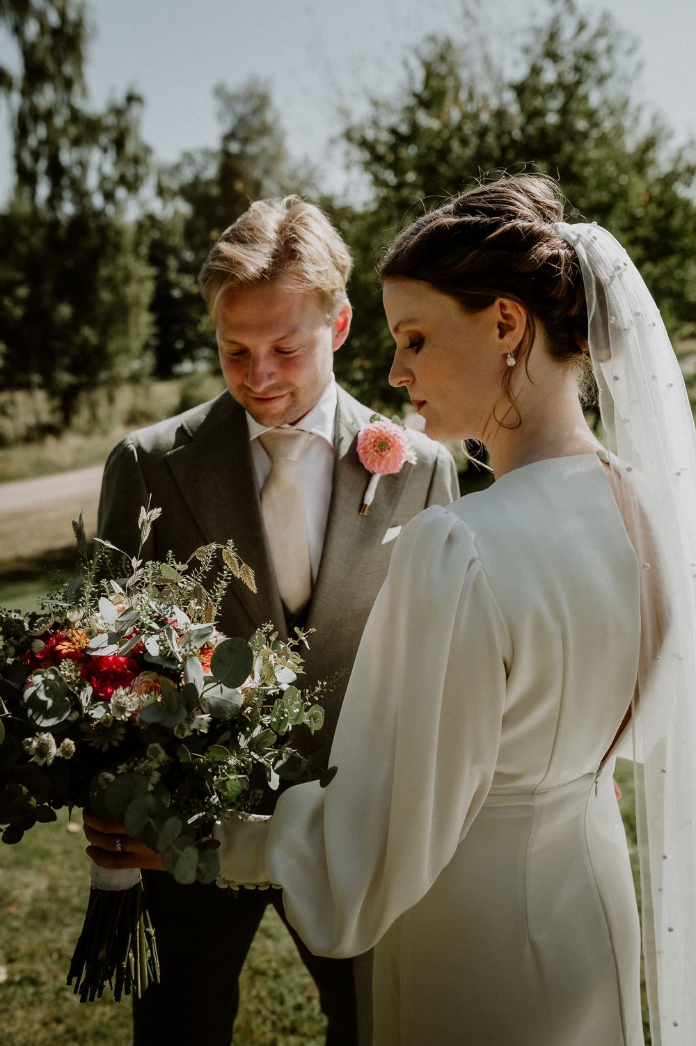 Brudpar står mitt emot varandra och tittar på brudbuketten.