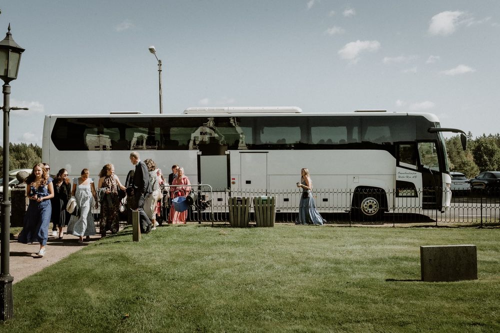 Bröllopsgäster anländer till kyrkan med buss. Bussen är vit.