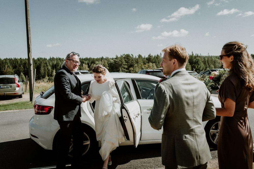 Brudpar anländer till Bjurbäcks kyrka för sin vigsel. Bruden får hjälp ut ur bilen av en man.