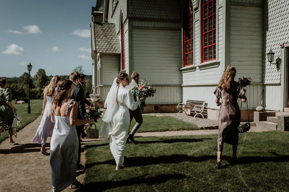 Brudpar och brudfölje på väg in i kyrka. Bruden håller sin brudbukett i handen.