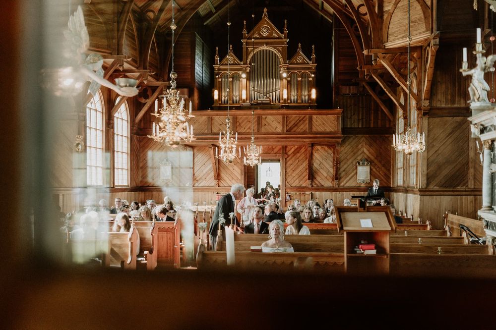 Bjurbäcks kyrka, Mullsjö. Väggarna är klädda med brunt trä. Bröllopsgäster börjar sätta sig i bänkarna.