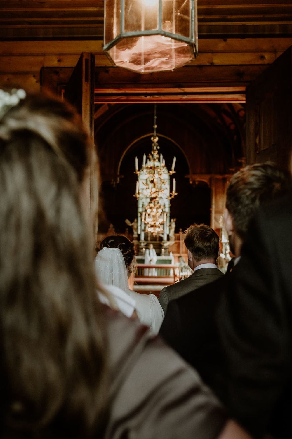 Brudpar på väg in i kyrkan. Dörrarna in i kyrksalen har precis öppnats och man ser brudparet och brudföljet bakifrån.